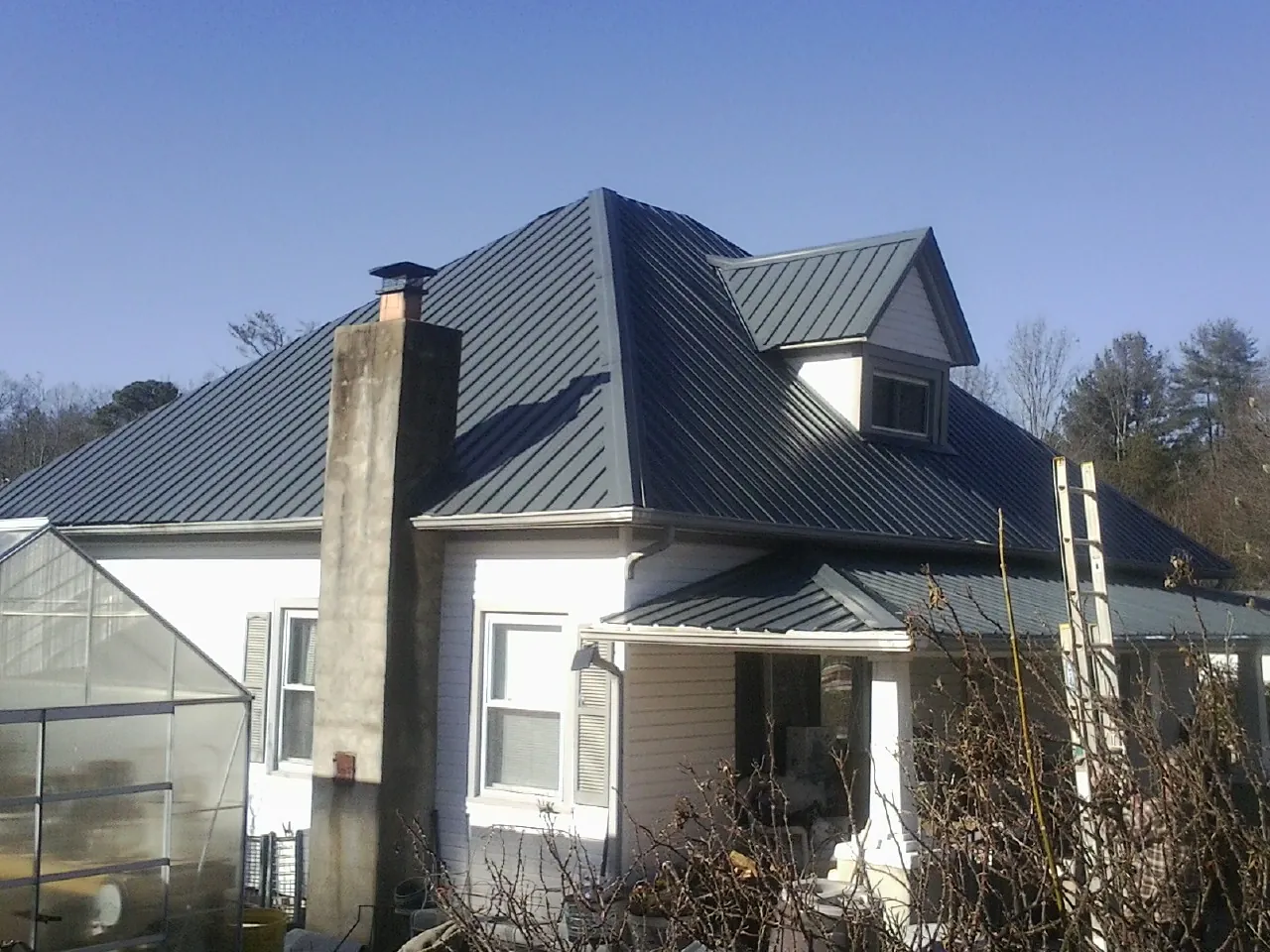 Dark blue standing seam metal roof on a white farmhouse with dormer — Slate & Tile Roof Repair by Roofing Brothers in Mount Morris