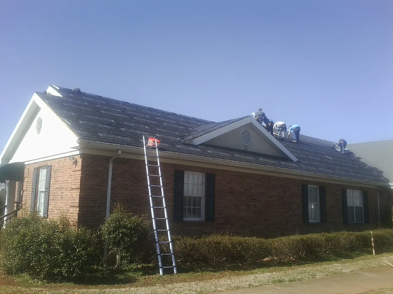 Crew tearing shingles off a brick ranch roof with a ladder set — Emergency Roof Repair work by our crew in Mount Morris