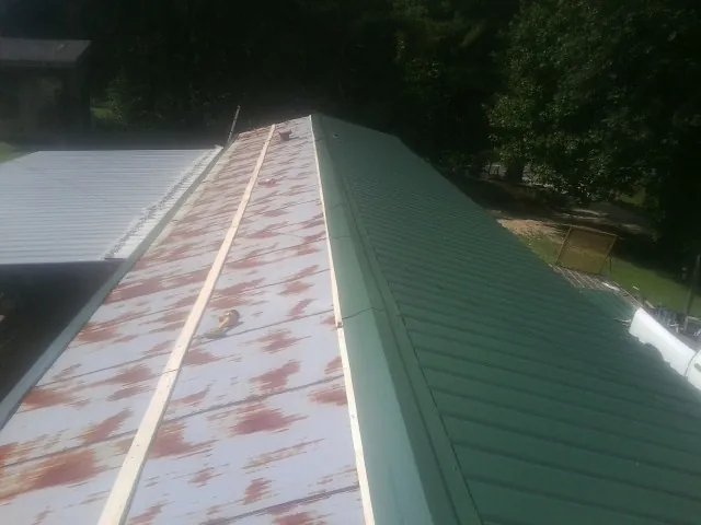 Old rusted panels beside newly installed green metal roofing — Wind Damage Roof Repair by Roofing Brothers in Mount Morris