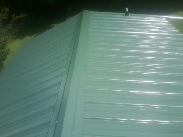 New green metal panels meeting at the ridge of a roof — Flat Roof Repair work by our crew in Mount Morris
