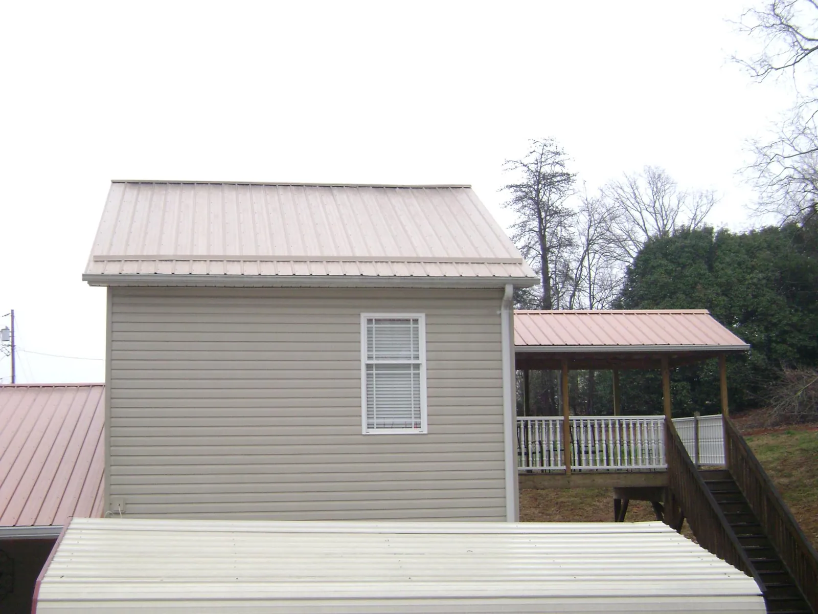 Tan metal roofs on a two story addition and attached porch, from a Roof Replacement job in Mount Morris